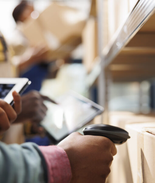 African american distribution warehouse worker arm scanning cardboard box code. Logistics manager cheking goods in stock using barcode scanner on freight parcels in storehouse